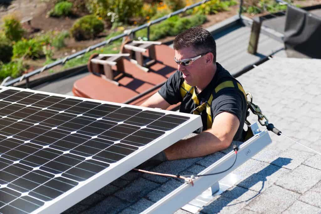 Solar installer wiring a solar panel on top of a roof.