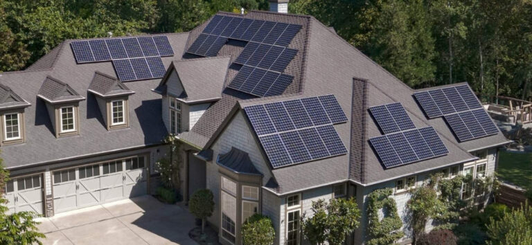 A large house with multiple solar panels installed on its roof, surrounded by trees and a landscaped yard.